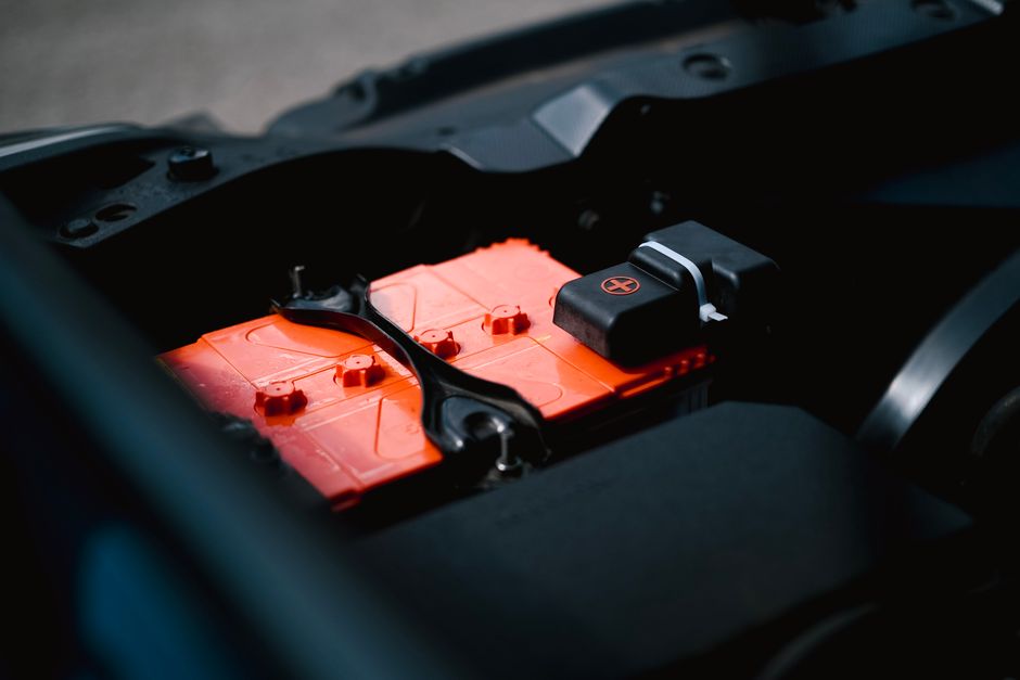 Detailed view of an orange car battery inside a vehicle&rsquo;s engine bay, highlighting its features.